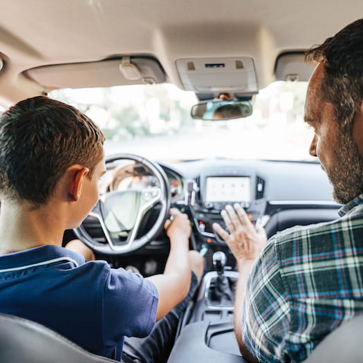 Teenager in driver's seat of vehicle with man providing instruction